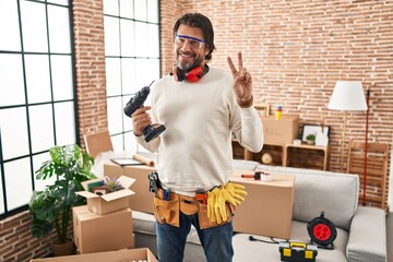 Handsome middle age man holding screwdriver at new home smiling with happy face winking at the...