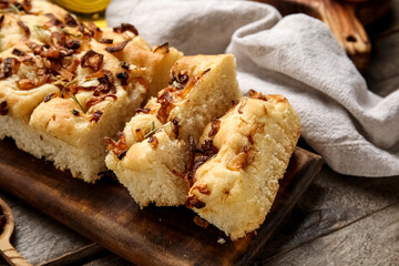 Board of tasty Italian focaccia with roasted onion on wooden table, closeup