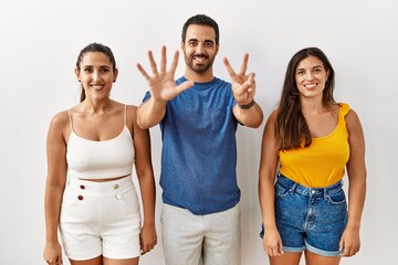 Group of young hispanic people standing over isolated background showing and pointing up with fingers number seven while smiling confident and happy.