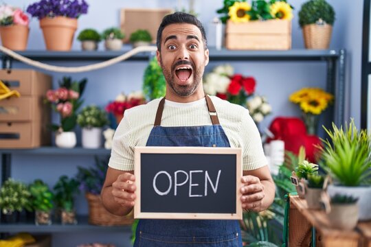 Hispanic man with beard working at florist holding open sign celebrating crazy and amazed for success with open eyes screaming excited.