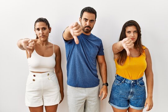 Group of young hispanic people standing over isolated background looking unhappy and angry showing rejection and negative with thumbs down gesture. bad expression.