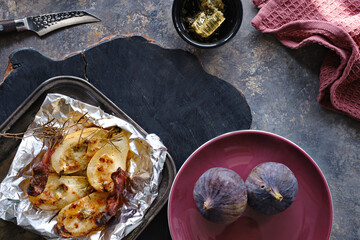 Baked pears with bacon, honey and red pepper. Flat lay, top view with fresh fig fruits and red towel on dark textured background.
