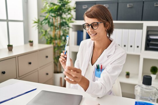 Young beautiful hispanic woman dentist holding electrical toothbrush and teethbrush at clinic