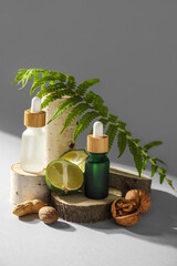 Fototapeta na wymiar Composition with bottles of essential oil, walnuts, lime and fern leaf on light background