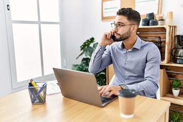 Young arab man talking on the smartphone using laptop working at office