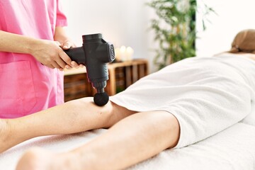 Middle age caucasian woman having legs massage using percussion pistol at beauty center