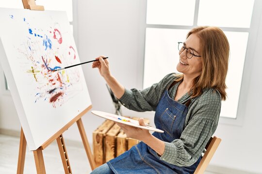 Middle age artist woman smiling happy painting at art studio.