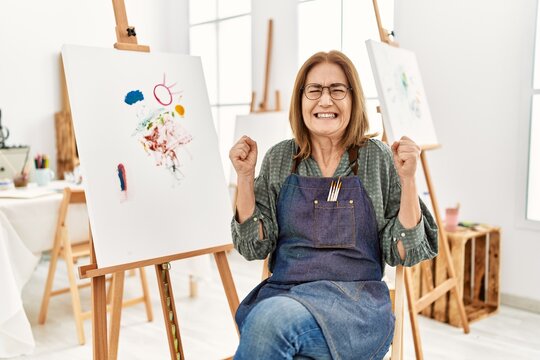 Middle age artist woman at art studio excited for success with arms raised and eyes closed celebrating victory smiling. winner concept.