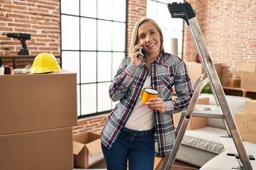 Young blonde woman talking on smartphone drinking coffee at new home