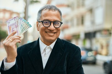 Middle age southeast asian man holding indian rupees banknotes at the city