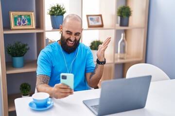 Fototapeta na wymiar Young hispanic man with beard and tattoos doing video call with smartphone screaming proud, celebrating victory and success very excited with raised arm