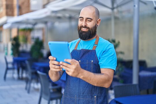 Young bald man waiter smiling confident using touchpad at coffee shop terrace