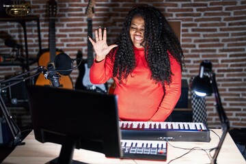 Plus size hispanic woman playing piano at music studio showing and pointing up with fingers number five while smiling confident and happy.