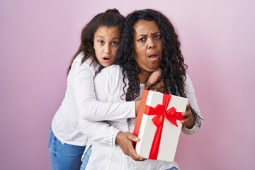 Mother and young daughter holding with presents in shock face, looking skeptical and sarcastic, surprised with open mouth