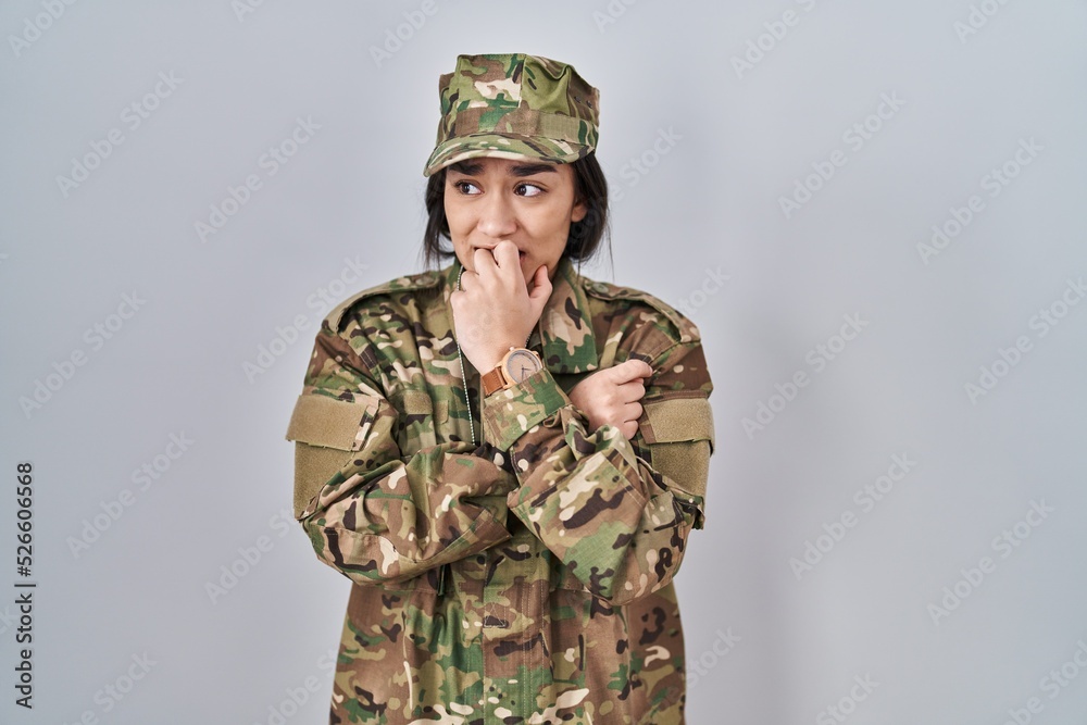 Poster young south asian woman wearing camouflage army uniform looking stressed and nervous with hands on m