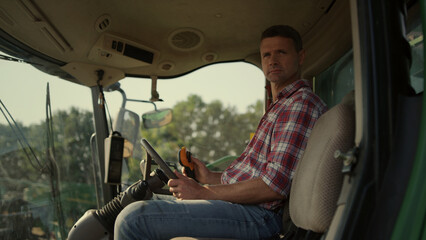 Farmer working tractor cabin at agricultural field. Man observing grain farmland