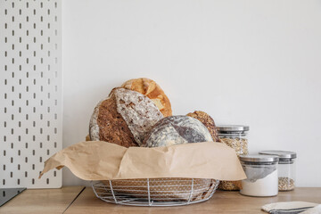 Basket with loaves of fresh bread, parchment paper and jars on kitchen counter near light wall