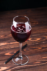 red cold summer alcoholic cocktail in a wine glass on wooden table.