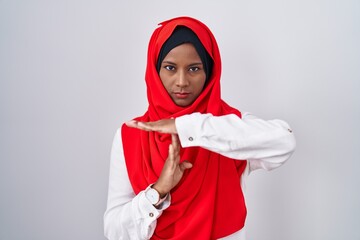 Young arab woman wearing traditional islamic hijab scarf doing time out gesture with hands,...