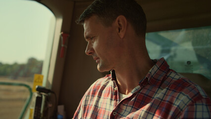 Combine driver working cabin in farmland closeup. Focused man checking harvester