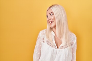 Caucasian woman standing over yellow background looking away to side with smile on face, natural expression. laughing confident.