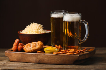 Board with glasses of beer and traditional food on table against dark background. Oktoberfest celebration