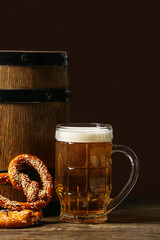 Mug of fresh beer with pretzels and barrel on table against dark background. Oktoberfest celebration