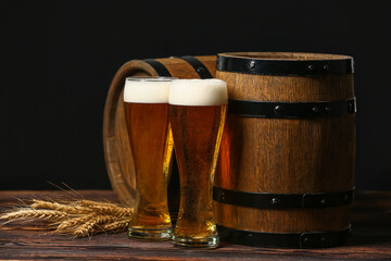 Glasses of fresh beer with spikelets and barrels on table against dark background. Oktoberfest...