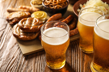Mugs of fresh beer and traditional food on wooden background, closeup. Oktoberfest celebration