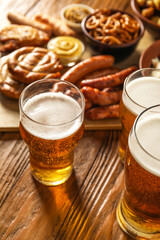Mugs of fresh beer and traditional food on wooden background, closeup. Oktoberfest celebration