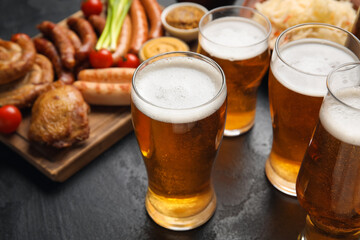 Mugs of fresh beer and traditional food on dark background, closeup. Oktoberfest celebration