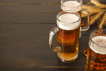 Mugs of fresh beer, pretzels and spikelets on wooden background, closeup. Oktoberfest celebration