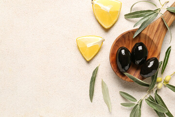 Composition with wooden spoon of tasty black olives, leaves and lemon pieces on light background
