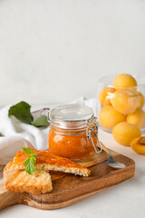 Wooden board of tasty sandwiches with apricot jam on light background