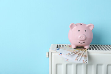 Piggy bank and euro banknotes on heating radiator against light blue background, space for text