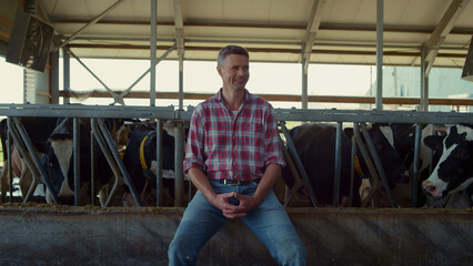 Fototapeta premium Happy farmer sitting cowshed feeder. Agro worker enjoying work process in barn.