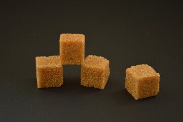 on a dark background lie a pyramid of sazar pieces of cane brown sugar.