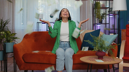 Money cash hundred euro rain falling on girl celebrating success, winning, goal achievement, good news, lottery jackpot luck at modern home office apartment indoors. Career grow. Woman sits on sofa