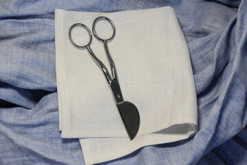 Small scissors lie on a linen napkin in the studio. A tool for hobby and tailoring. Clean and sharpen the blades.