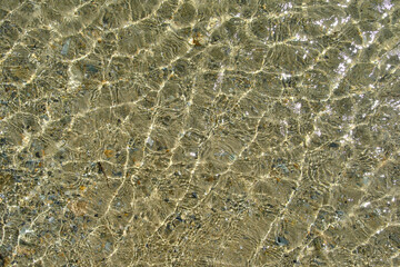 The sandy bottom of the sea with the purest transparent water with sun glare on the waves. Abstract background.