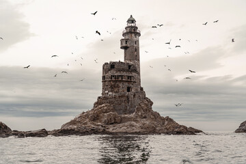 An old crumbling, very beautiful and high lighthouse, on a rock in the open sea, around which gulls and other birds circle in flocks. The grandeur of the past, the incredibly beautiful landscape