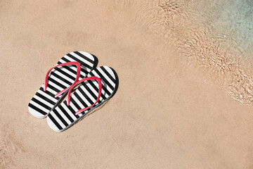 Fototapeta na wymiar Stylish flip flops on sandy beach near sea, above view. Space for text