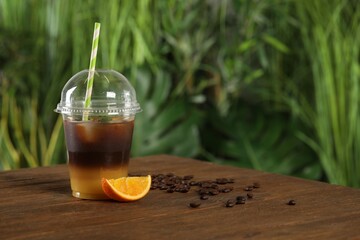 Tasty refreshing drink with coffee and orange juice in plastic cup on wooden table against blurred...