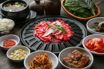 Bulgogi, a traditional Korean food on a black stone plate with a wooden background, and side dishes 나무배경에 검은 돌판위에 있는 한국 전통 음식인 불고기와 밑반찬