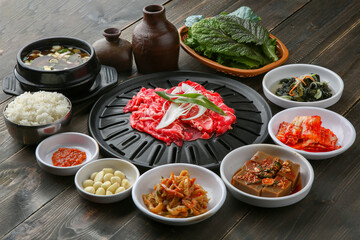 Bulgogi, a traditional Korean food on a black stone plate with a wooden background, and side dishes 나무배경에 검은 돌판위에 있는 한국 전통 음식인 불고기와 밑반찬