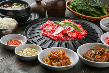 Bulgogi, a traditional Korean food on a black stone plate with a wooden background, and side dishes 나무배경에 검은 돌판위에 있는 한국 전통 음식인 불고기와 밑반찬