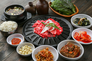 Bulgogi, a traditional Korean food on a black stone plate with a wooden background, and side dishes 나무배경에 검은 돌판위에 있는 한국 전통 음식인 불고기와 밑반찬
