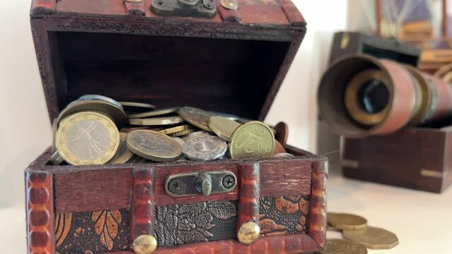 A chest filled with coins, it is ajar from it. Coins scattered in the background, a spyglass is visible, everything is on a white background. Brown wooden box Wealth income earnings saving money.