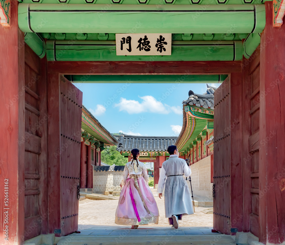 Wall mural couple wearing traditional korean clothing hanbok by a colorful wooden temple entrance door design a