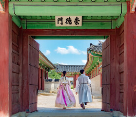 Couple wearing traditional Korean clothing hanbok by a colorful wooden temple entrance door design...